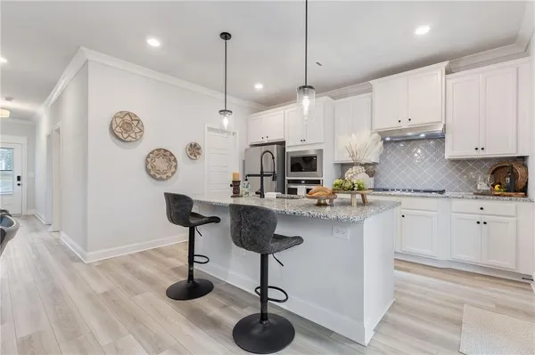 a kitchen with stainless steel appliances kitchen island a refrigerator a stove and white cabinets with wooden floor