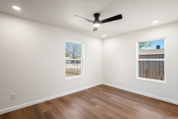 an empty room with wooden floor ceiling fan and windows