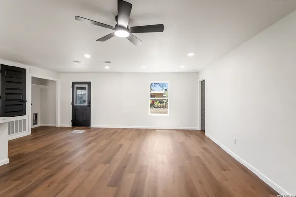an empty room with wooden floor chandelier fan and windows