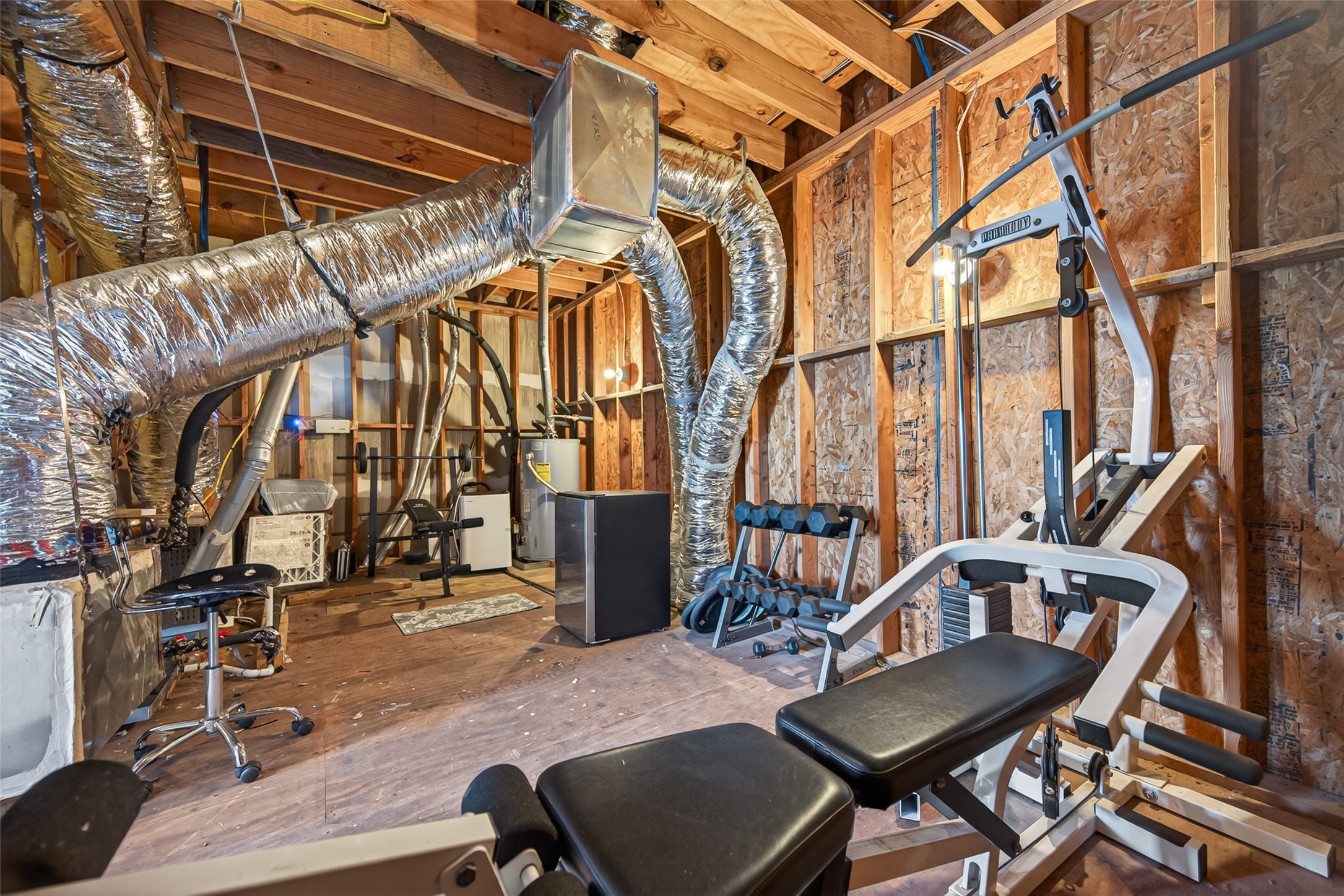2611 Riverside Drive, Unit C Houston, TX 77004 - Photo 46 of 50 This unfinished attic space features exposed ductwork and natural wood beams, offering a raw, industrial feel with incredible potential. Currently set up as a home gym with a weight machine and dumbbell rack, the area also houses utility components. With the right vision, this versatile space could be transformed into a custom bathroom, music studio, or content creation space tailored to your lifestyle.