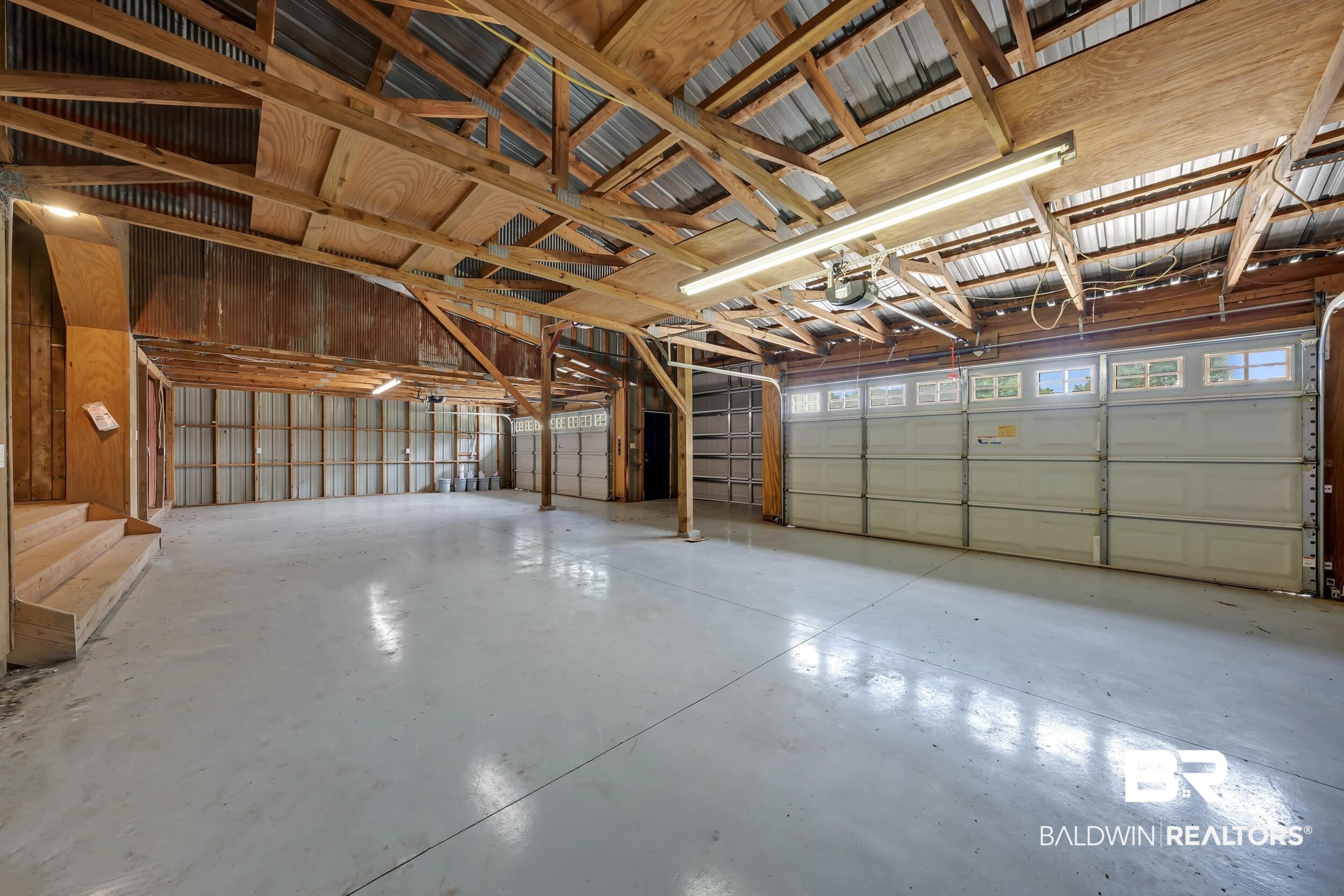 43199 Pine Grove Road Bay Minette, AL 36507 - Photo 25 of 71 Spacious multi-bay garage featuring a light gray finished concrete floor, exposed wood beam ceiling, corrugated metal walls, and overhead fluorescent lighting