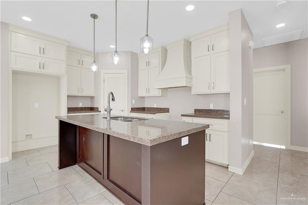 824 Lark Street Alamo, TX 78516 - Photo 7 of 17 Kitchen featuring dark stone counters, custom exhaust hood, an island with sink, hanging light fixtures, and light tile patterned floors