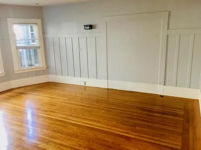 a view of an empty room with wooden floor and a window