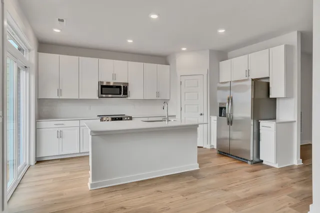 a kitchen with stainless steel appliances granite countertop a refrigerator a stove a sink and white cabinets with wooden floor