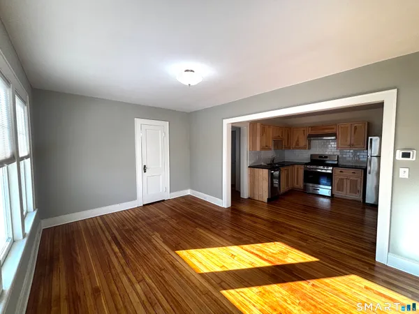 a view of empty room with wooden floor and kitchen view