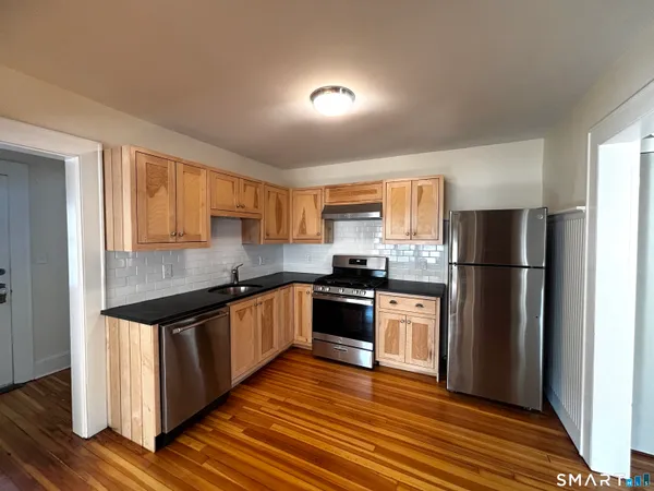 a kitchen with stainless steel appliances granite countertop a refrigerator a sink dishwasher a stove and white countertops with wooden floor