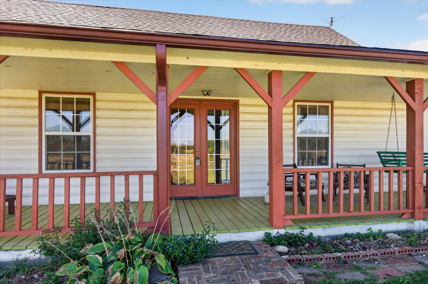 26115 4157th Road Nowata, OK 74048 - Photo 3 of 36 Charming farmhouse-style residence featuring a wraparound covered porch with red timber framing and white railings, cream-colored horizontal siding, and multiple multi-pane windows