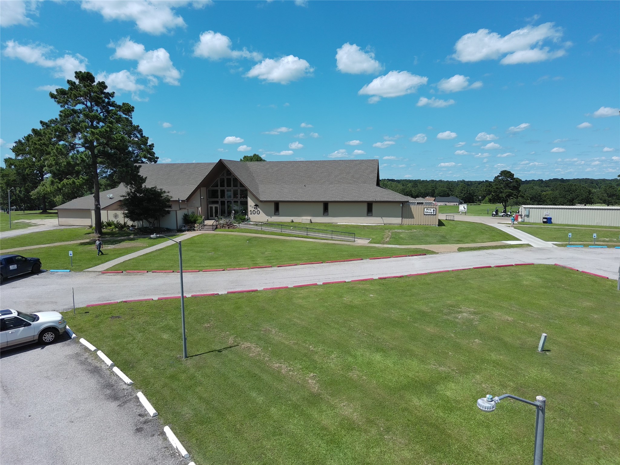 59 Oakridge South Trinity, TX 75862 - Photo 9 of 10 This photo shows a large, modern building with a sloped roof set in a spacious, grassy area. The property features a well-maintained lawn, ample parking, and is surrounded by trees, offering a peaceful and open environment.
