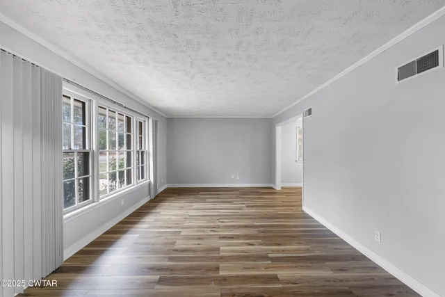 a view of an empty room with wooden floor and a window