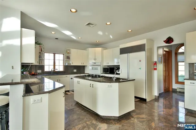 a kitchen with stainless steel appliances granite countertop a stove top oven a sink a refrigerator and white cabinets