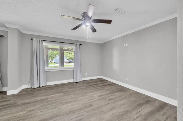 an empty room with wooden floor fan and windows