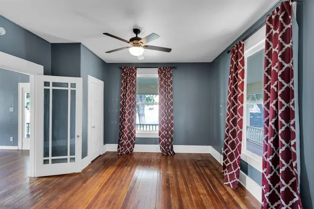a view of an empty room with wooden floor and fan