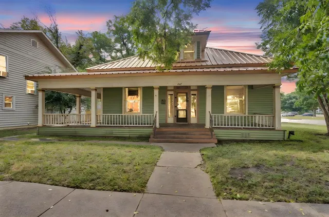 a view of a house with a yard plants and large tree