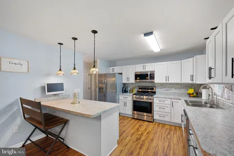 a kitchen with stainless steel appliances a stove a sink a microwave a refrigerator a stove and white cabinets