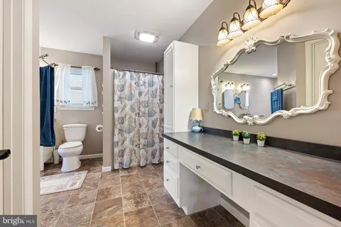 a spacious bathroom with a granite countertop sink a toilet a mirror and shower