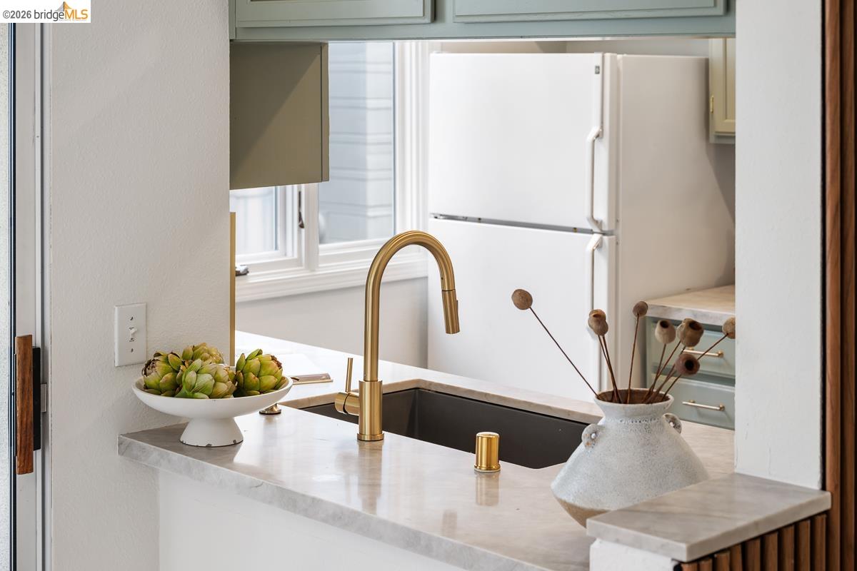 2029 Channing Way, Unit 3D Berkeley, CA 94704 - Photo 20 of 54 Kitchen pass-through featuring a deep-set sink with a brass-finish faucet, light-toned countertop, and light green cabinetry