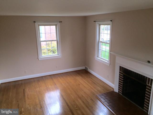 3014 Dunmurry Road Baltimore, MD 21222 - Photo 6 of 24 an empty room with wooden floor a fireplace and windows