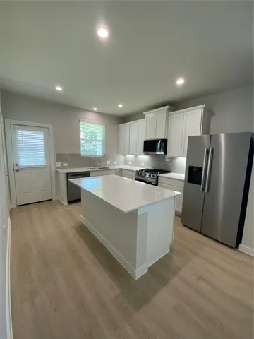 a large kitchen with stainless steel appliances granite countertop a stove a refrigerator a sink a microwave and white cabinets