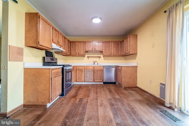 a kitchen with wooden floors stainless steel appliances a sink and a window