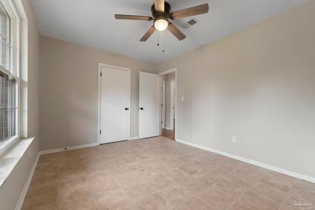 an empty room with chandelier fan and windows