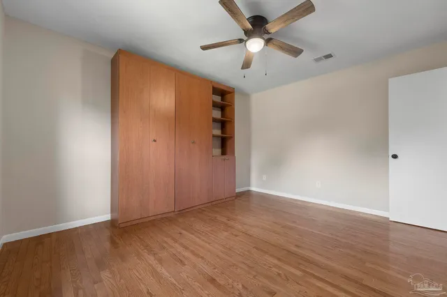 an empty room with wooden floor chandelier fan and closet area with wooden floor