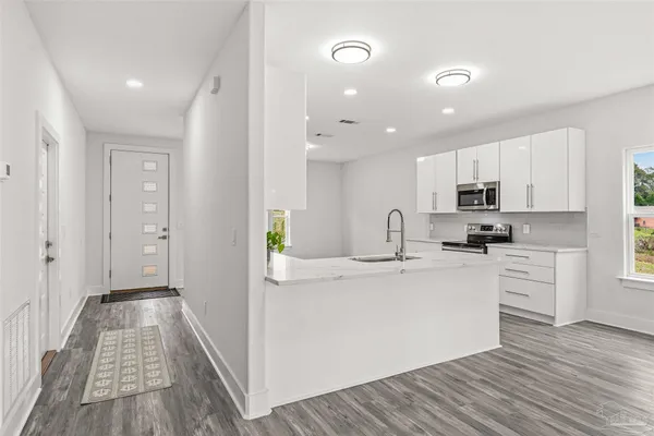 a view of a kitchen with kitchen island a sink wooden floor and stainless steel appliances
