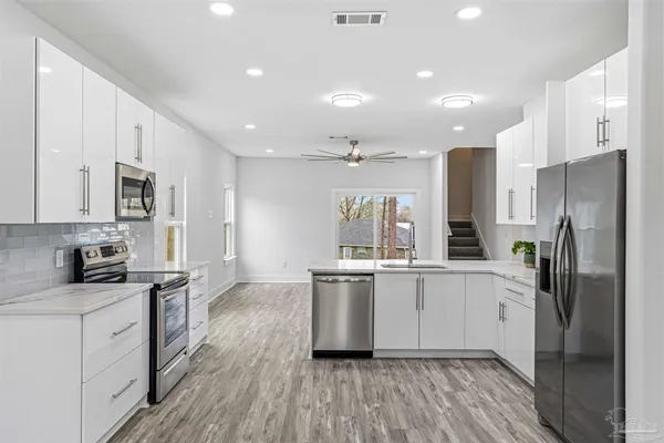 a kitchen with stainless steel appliances a refrigerator a sink dishwasher a stove top oven a refrigerator and white cabinets with wooden floor