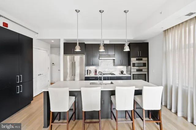 a kitchen with stainless steel appliances kitchen island granite countertop a dining table chairs and a refrigerator