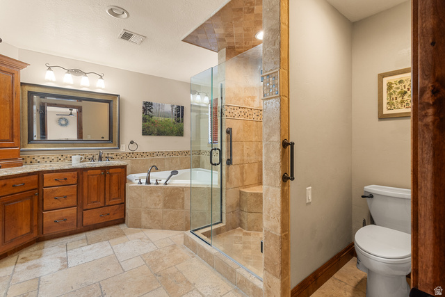 892 Cambridge Drive St. George, UT 84770 - Photo 50 of 65 Spacious bathroom featuring a glass-enclosed shower with stone tile, a built-in tub with stone surround, a dual vanity with wood cabinetry and light-toned countertops, and neutral tile flooring