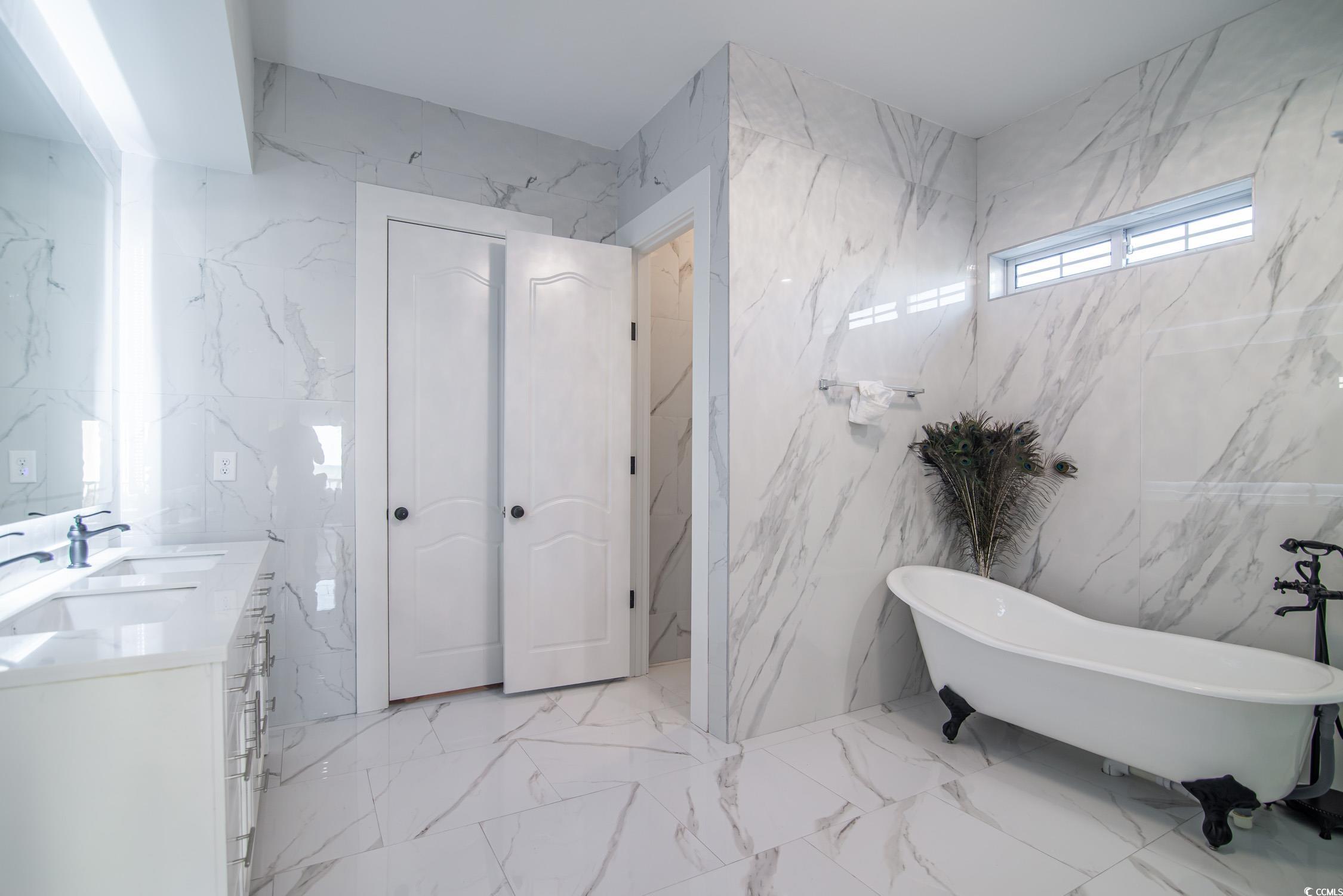 139 Pioneer Loop Georgetown, SC 29440 - Photo 19 of 39 Full bath featuring stone wall, double vanity, a freestanding bath, tile walls, and light marble finish flooring