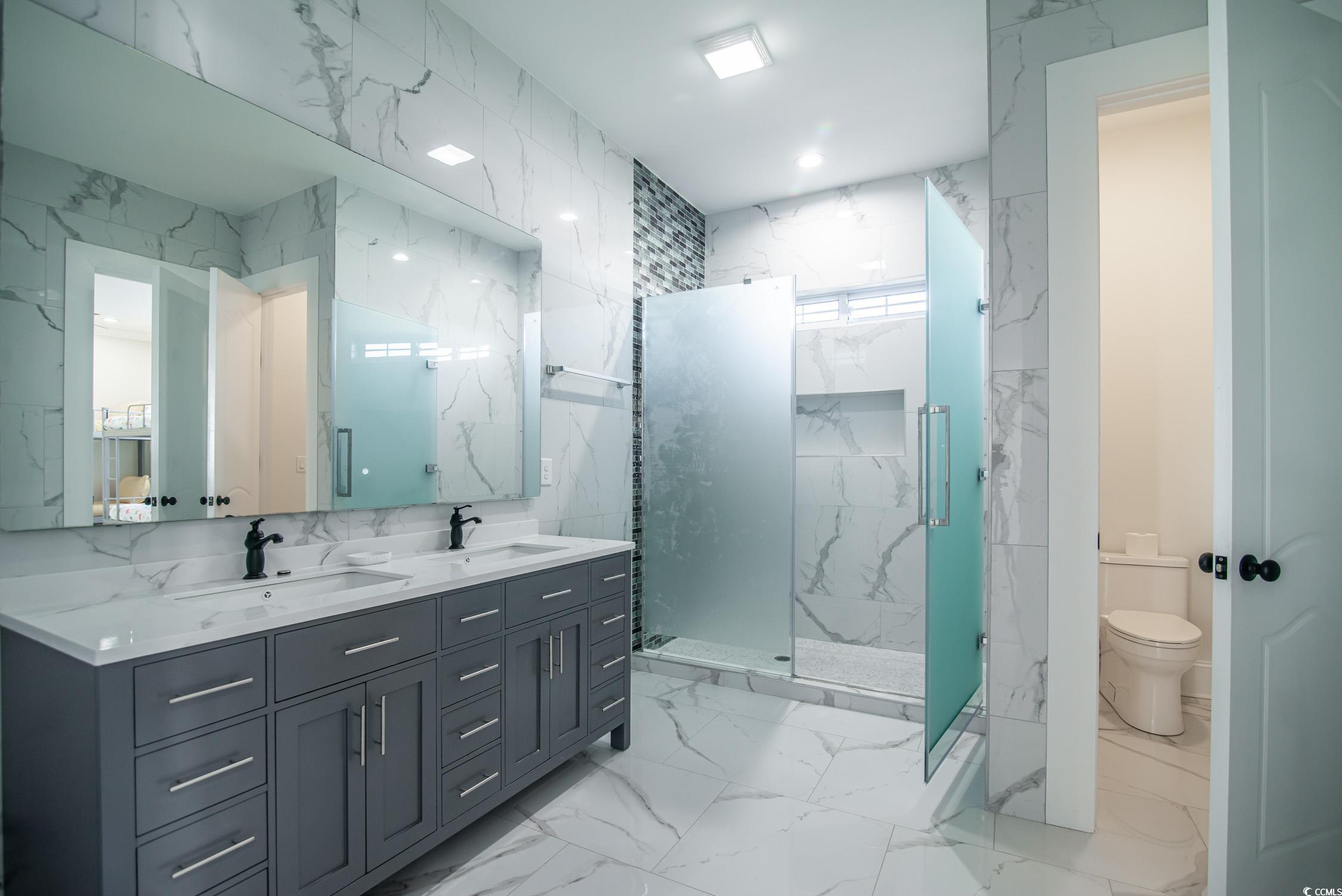 139 Pioneer Loop Georgetown, SC 29440 - Photo 26 of 39 Bathroom with tile walls, stone wall, light marble finish flooring, a marble finish shower, and double vanity