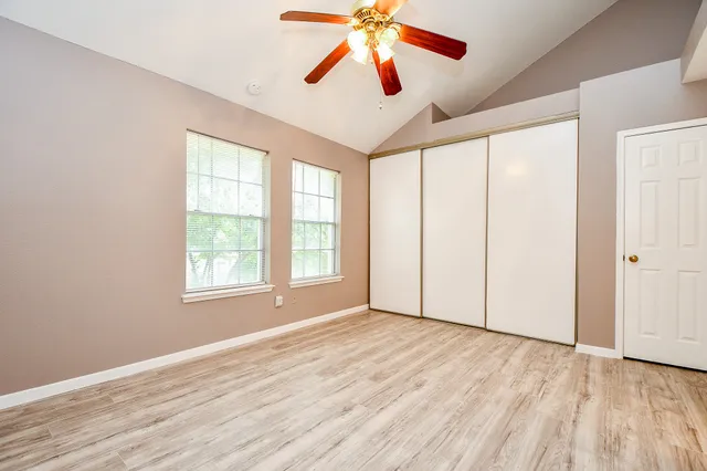 an empty room with wooden floor chandelier fan and windows
