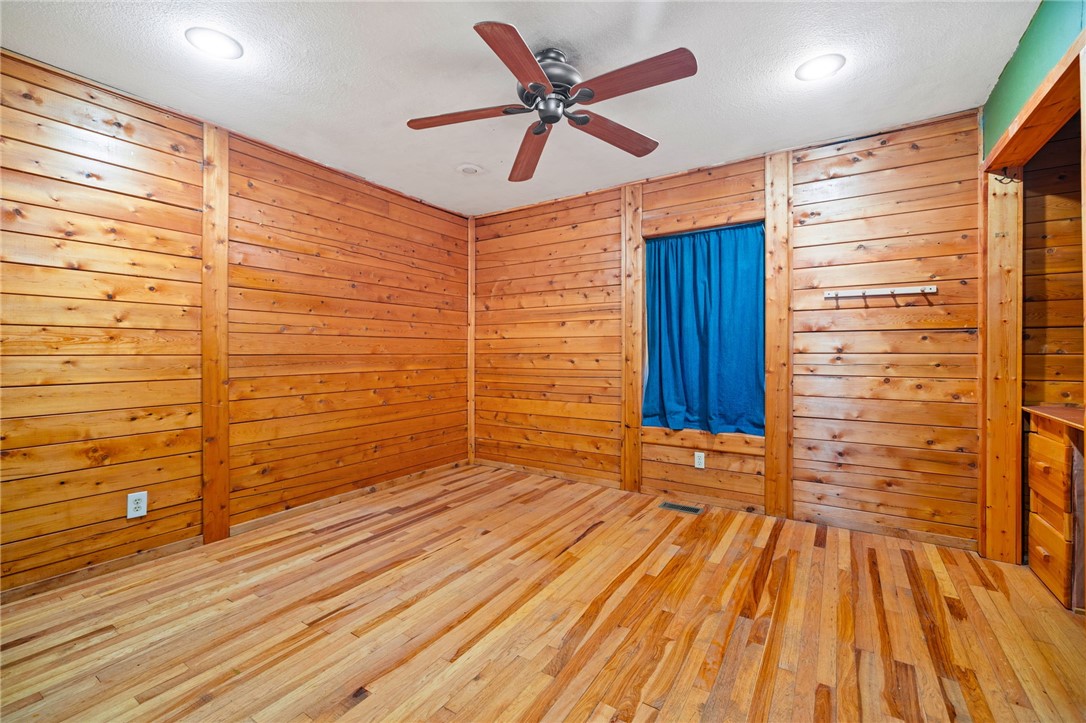 10557 North Devils Den Road Winslow, AR 72959 - Photo 25 of 60 Empty room featuring hardwood / wood-style flooring, a ceiling fan, wooden walls, and a textured ceiling