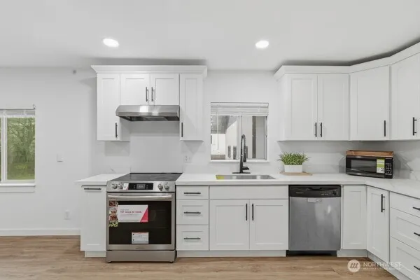 a view of an empty room and kitchen with wooden floor