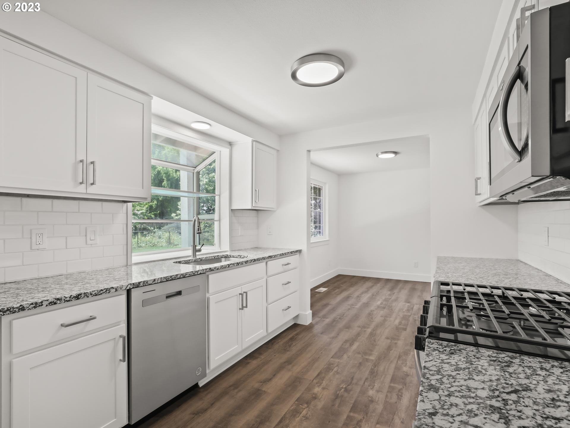 19650 Southwest Celebrity Street Beaverton, OR 97078 - Photo 10 of 47 a kitchen with granite countertop a stove a sink and dishwasher with wooden floor