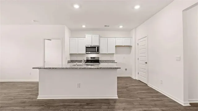 a large kitchen with stainless steel appliances granite countertop a stove a sink a refrigerator and white cabinets with wooden floor