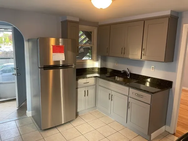 a kitchen with granite countertop a refrigerator a sink and white cabinets
