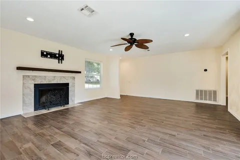 a view of an empty room with wooden floor fireplace and a window