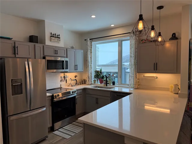 a kitchen with stainless steel appliances granite countertop a refrigerator a sink dishwasher a stove and white countertops with wooden floor