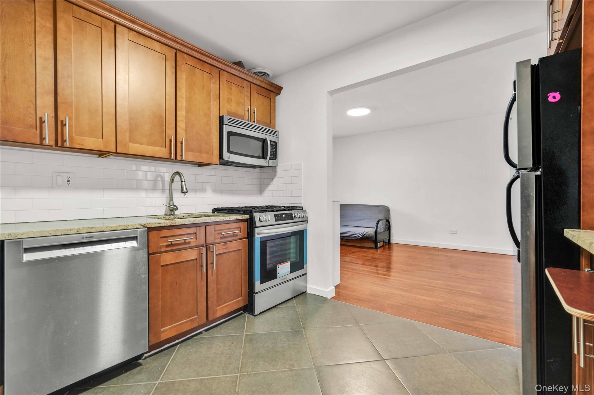 150-29 72nd Road, Unit 4H Queens, NY 11367 - Photo 9 of 16 a kitchen with stainless steel appliances granite countertop a stove a sink and a refrigerator