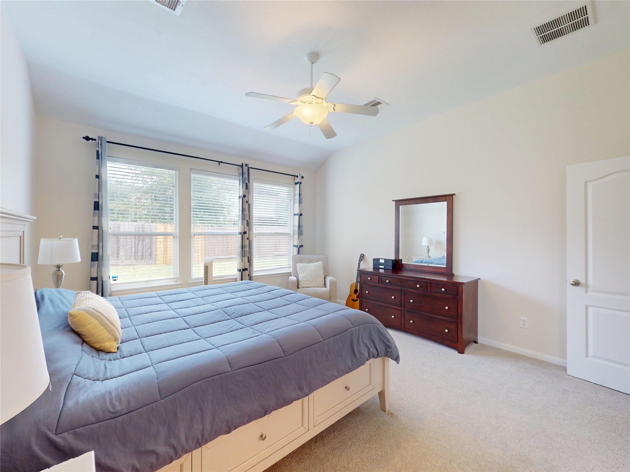 17402 Rainer Valley Lane Humble, TX 77346 - Photo 16 of 33 This spacious bedroom features a large bed, ample natural light from three windows, a ceiling fan, and neutral carpeting. It includes a wooden dresser with a mirror, a cozy chair, and a modern, inviting atmosphere.