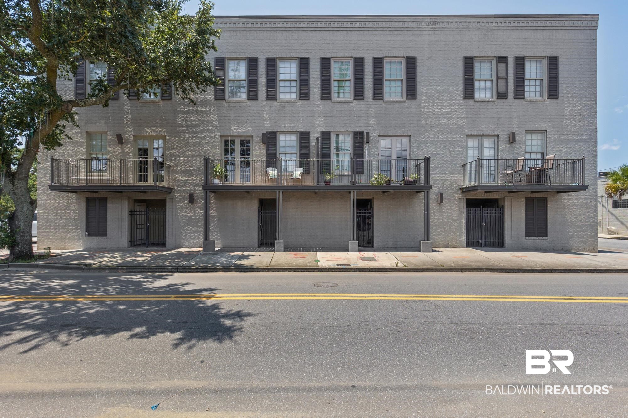 701 Dauphin Street, Unit A Mobile, AL 36602 - Photo 1 of 31 Three-story brick exterior featuring multiple private balconies, ground-level entryways, and traditional shuttered windows
