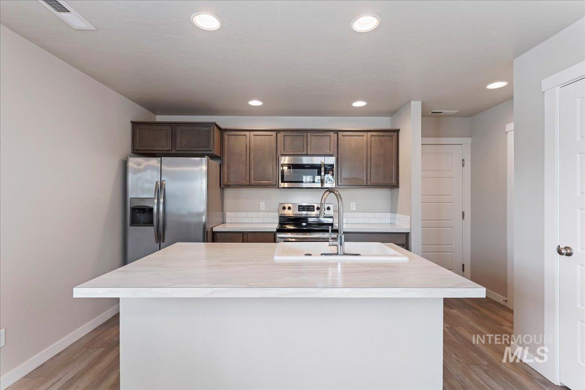 2517 East Goldstone Street Meridian, ID 83642 - Photo 9 of 22 Kitchen with stainless steel appliances, light countertops, a kitchen island with sink, recessed lighting, and dark wood finish cabinetry