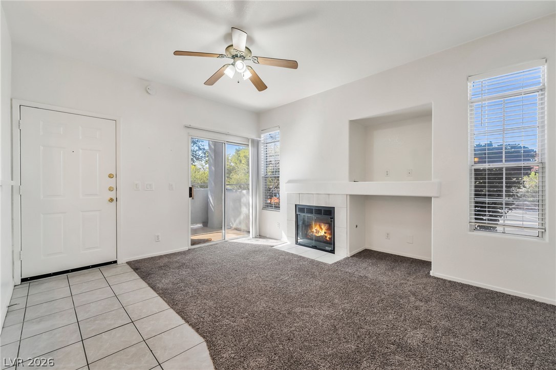 2201 Ramsgate Drive, Unit 811 Henderson, NV 89074 - Photo 4 of 36 A cozy living space features a tiled fireplace, a ceiling fan, and sliding doors opening to an outdoor area.
