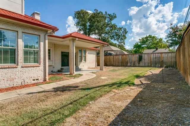 a view of a white house with a small yard plants and large tree
