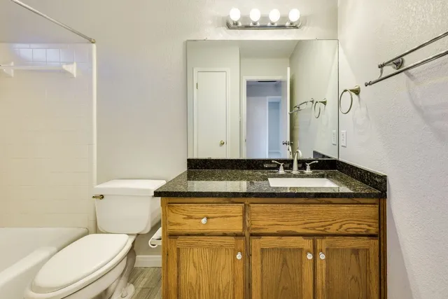 a bathroom with a granite countertop sink vanity mirror and toilet