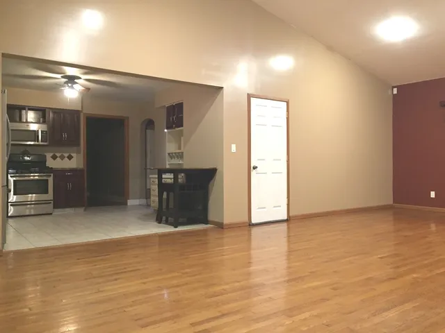 an empty room with wooden floor and way to kitchen