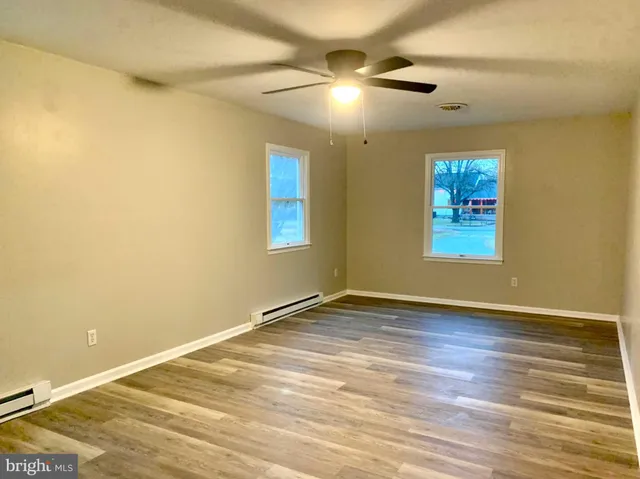 an empty room with wooden floor chandelier fan and windows