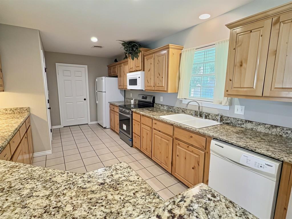 313 East River Oaks Road Early, TX 76802 - Photo 7 of 34 Kitchen featuring light wood cabinetry, stone-finish countertops, tile flooring, and white appliances