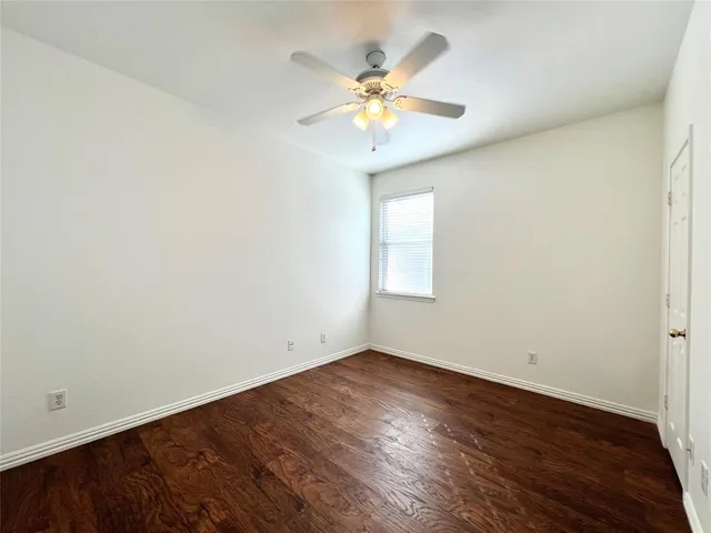 an empty room with wooden floor chandelier fan and windows